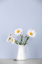 Beautiful tender chamomile flowers in jug on table against light background