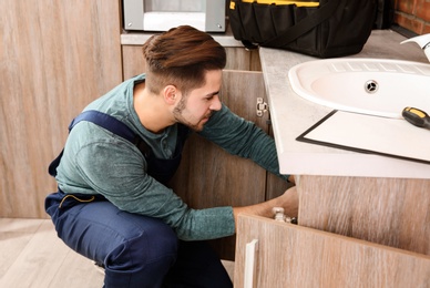 Male plumber in uniform repairing kitchen sink