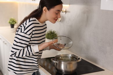 Photo of Beautiful woman smelling aromatic soup in kitchen. Space for text