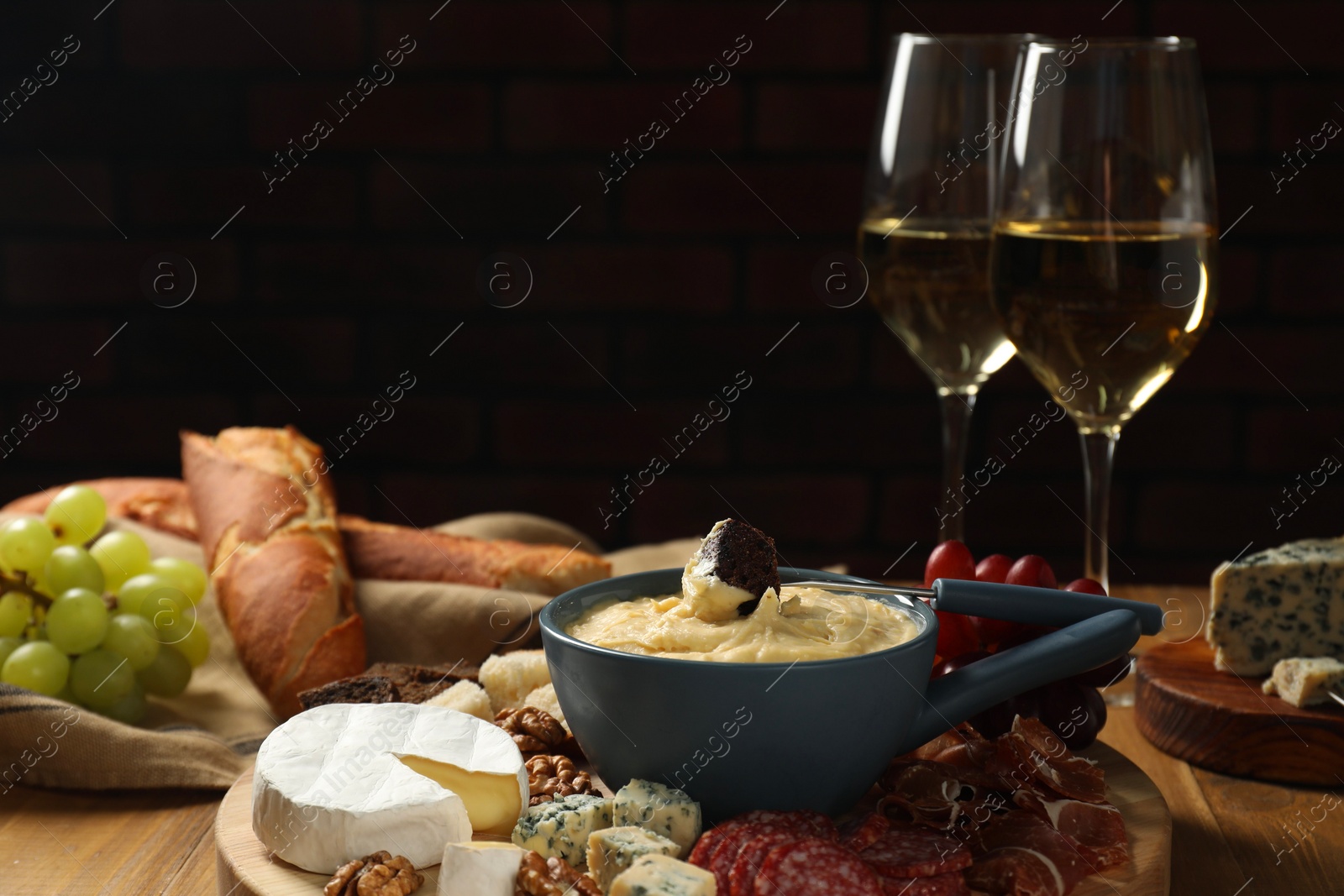 Photo of Fondue pot with tasty melted cheese, fork, different snacks and wine on wooden table