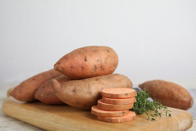 Photo of Wooden board with thyme and sweet potatoes on table