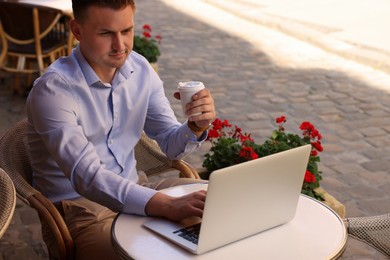 Photo of Handsome man with cup of coffee working on laptop at table in outdoor cafe