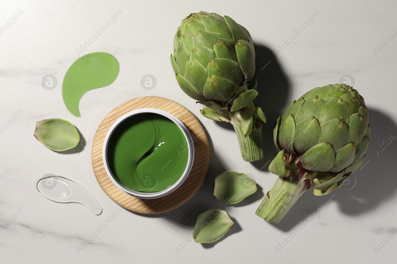 Photo of Package of under eye patches and artichokes on white marble table, flat lay. Cosmetic product