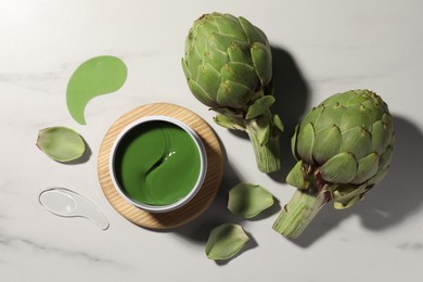 Photo of Package of under eye patches and artichokes on white marble table, flat lay. Cosmetic product