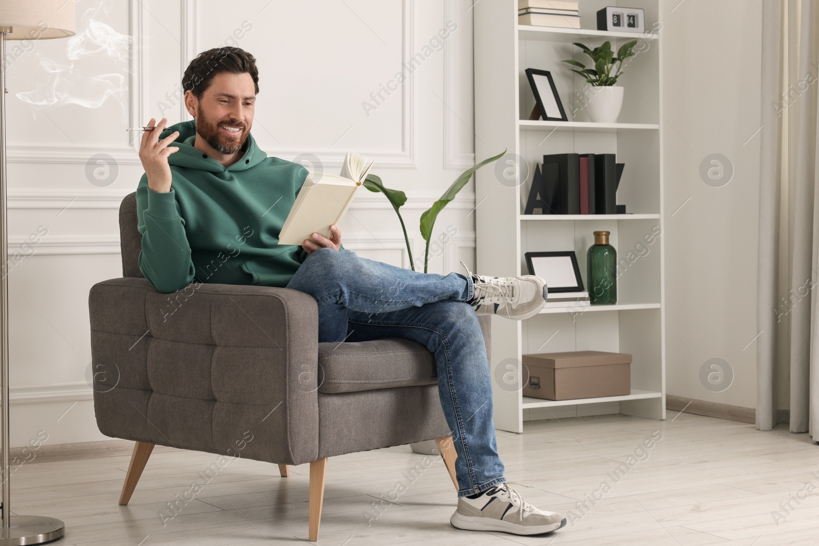 Photo of Man using cigarette holder for smoking white reading book indoors