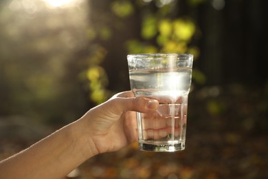 Photo of Woman holding glass of fresh water in forest on sunny day, closeup
