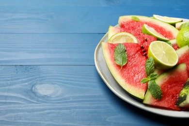 Photo of Plate with cut juicy watermelon and lime on blue wooden table, space for text
