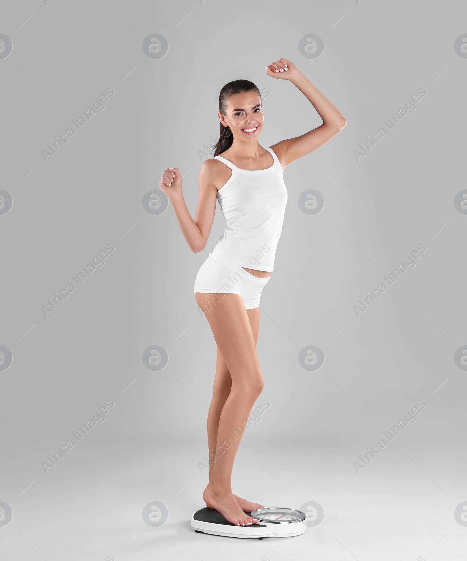 Photo of Happy young woman measuring her weight using scales on color background. Weight loss motivation