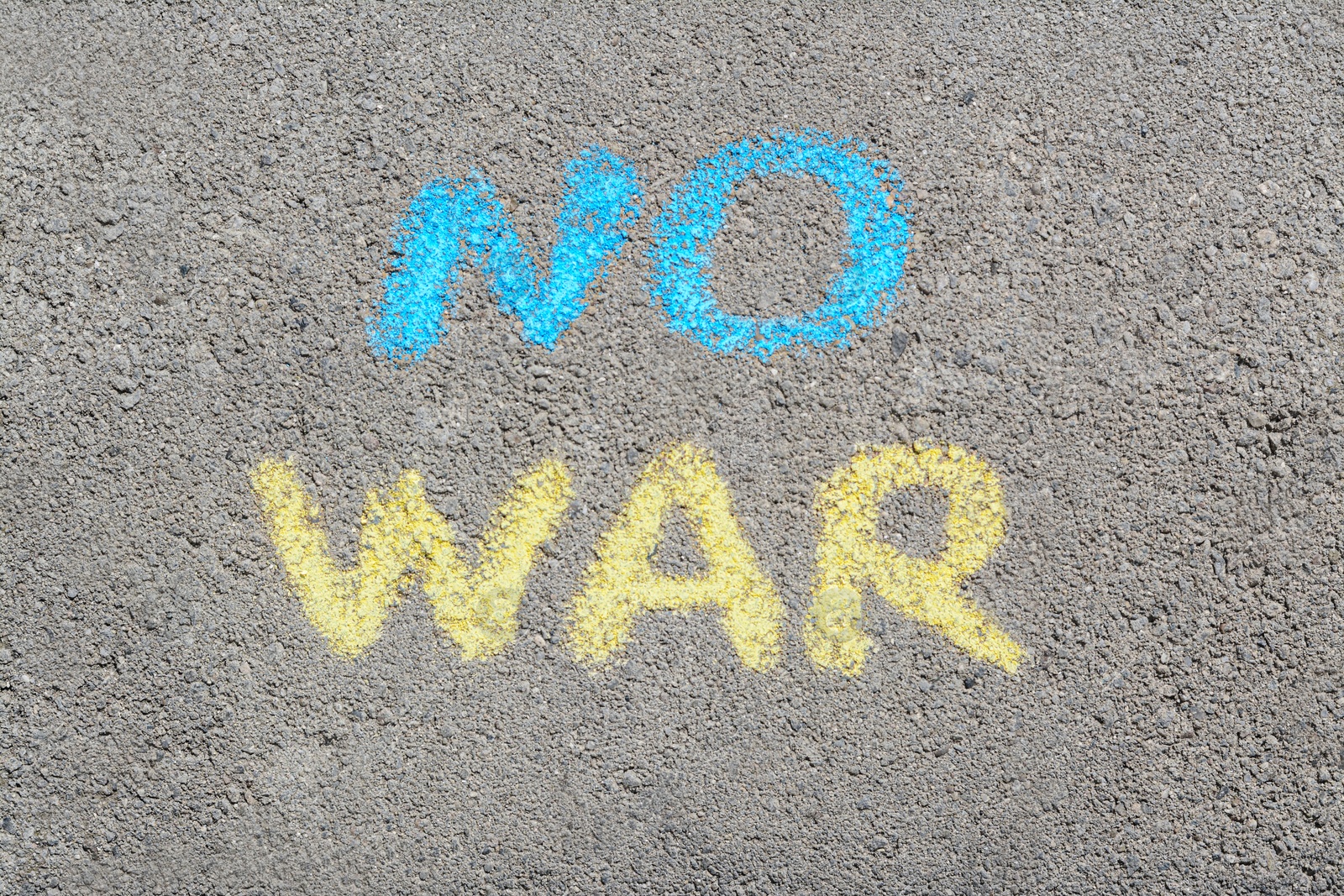 Photo of Words No War written with blue and yellow chalks on asphalt outdoors, top view