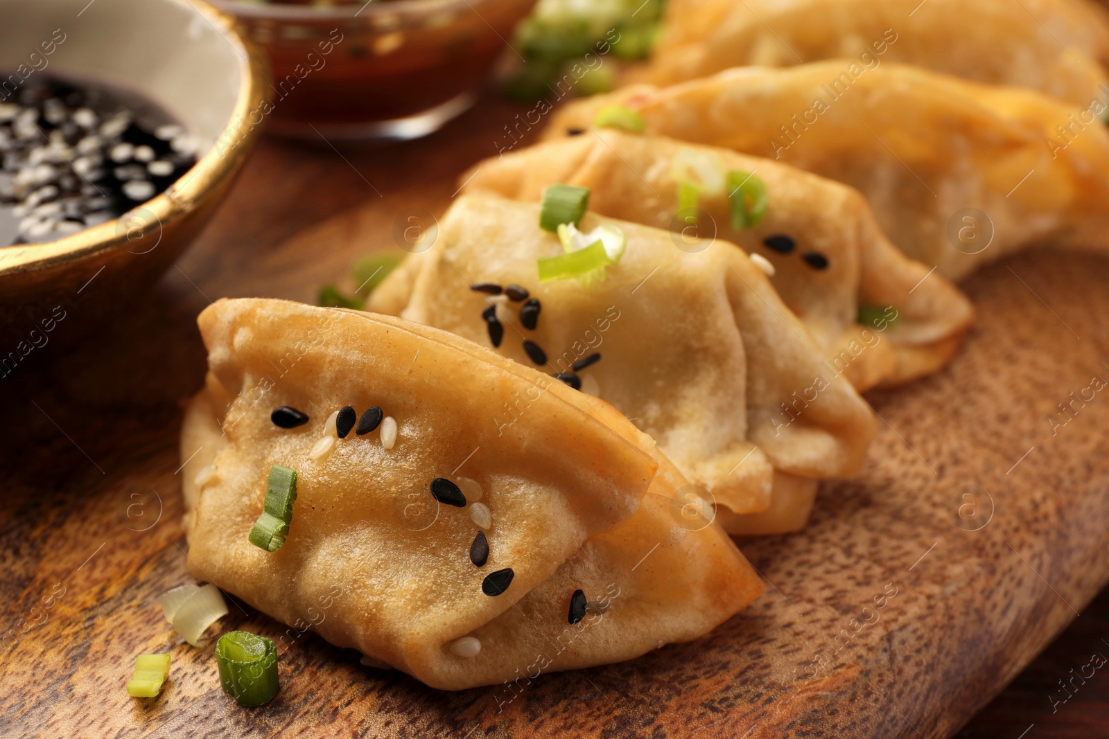 Photo of Delicious gyoza (asian dumplings) with sesame seeds and green onions on board, closeup