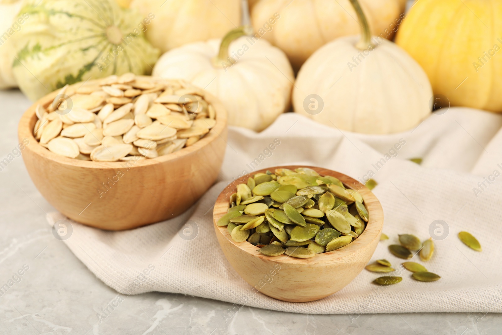 Photo of Wooden bowls with seeds and fresh pumpkins on grey marble table