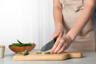 Photo of Woman cutting raw green beans for tasty dish at table