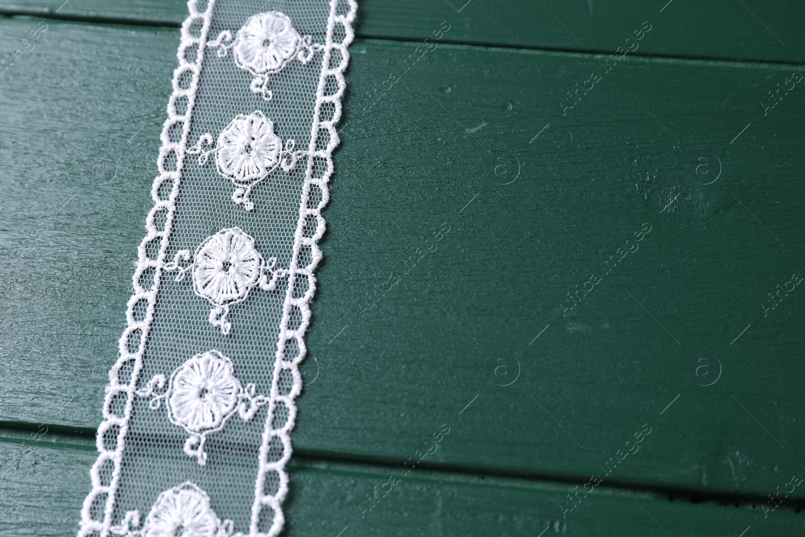 Photo of White lace on green wooden table, above view. Space for text