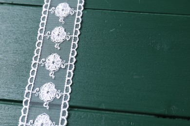 Photo of White lace on green wooden table, above view. Space for text