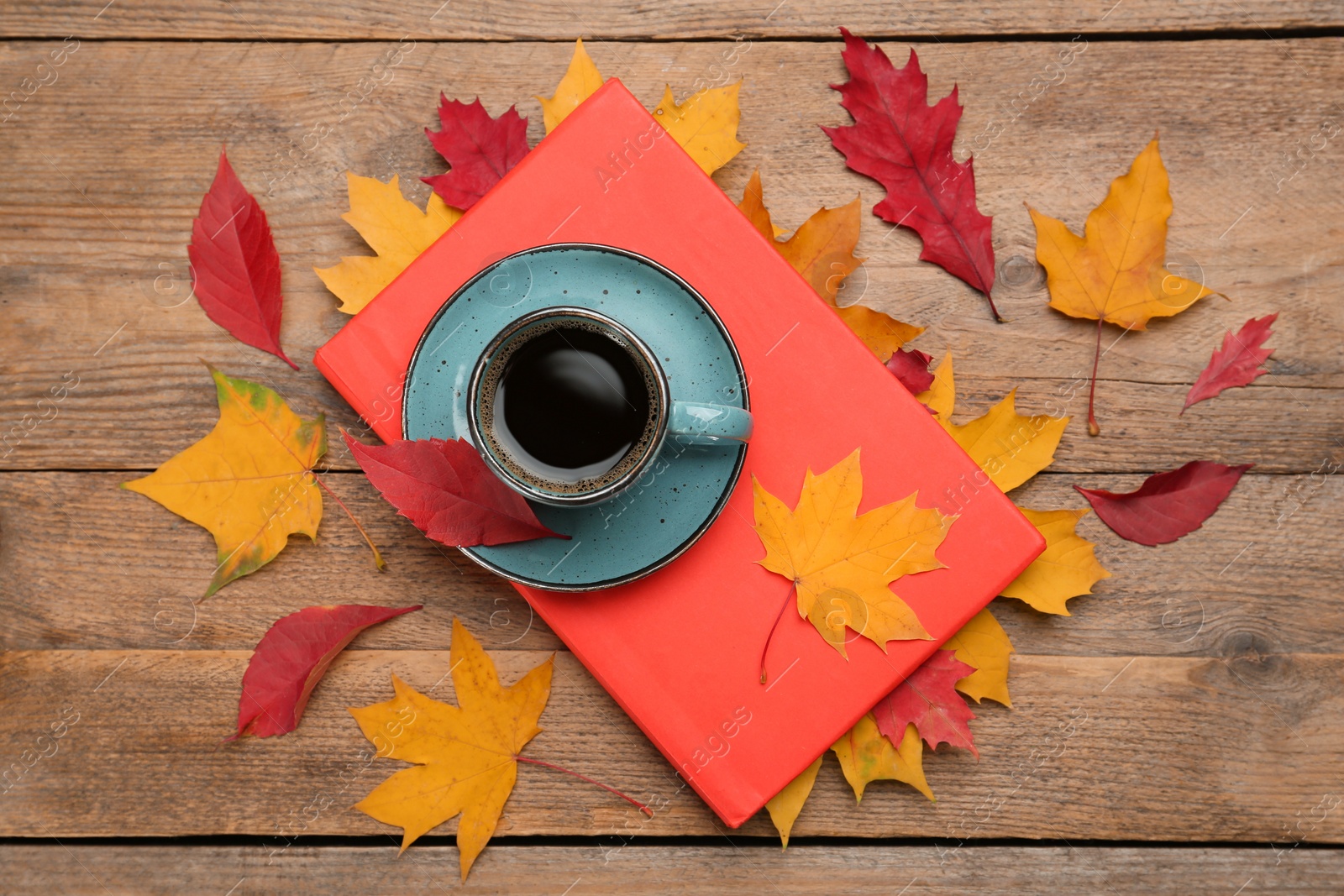 Photo of Cup of hot coffee, book and autumn leaves on wooden table, flat lay
