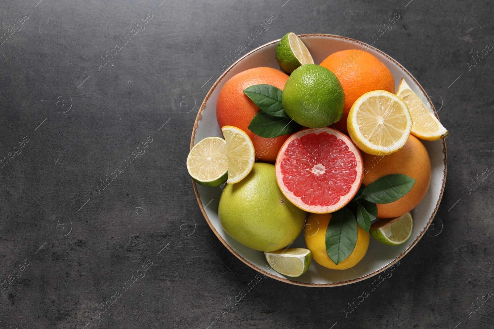 Photo of Different fresh citrus fruits and leaves on grey textured table, top view. Space for text