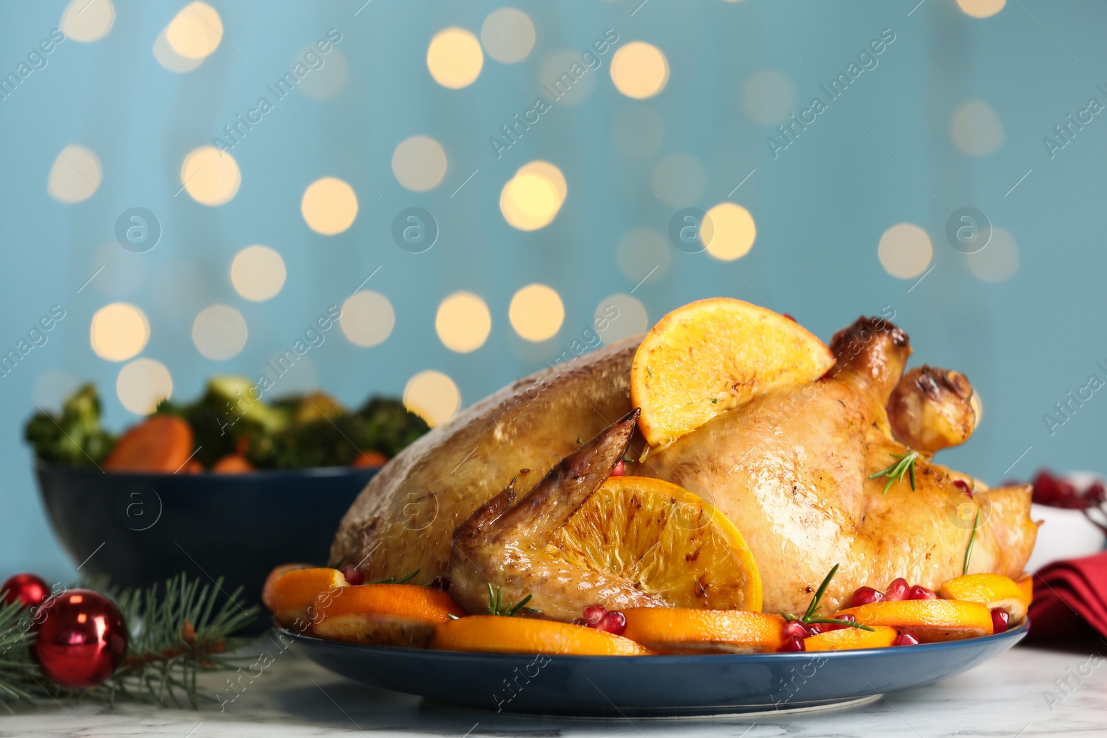 Photo of Delicious chicken with oranges and pomegranate on white table against blurred festive lights