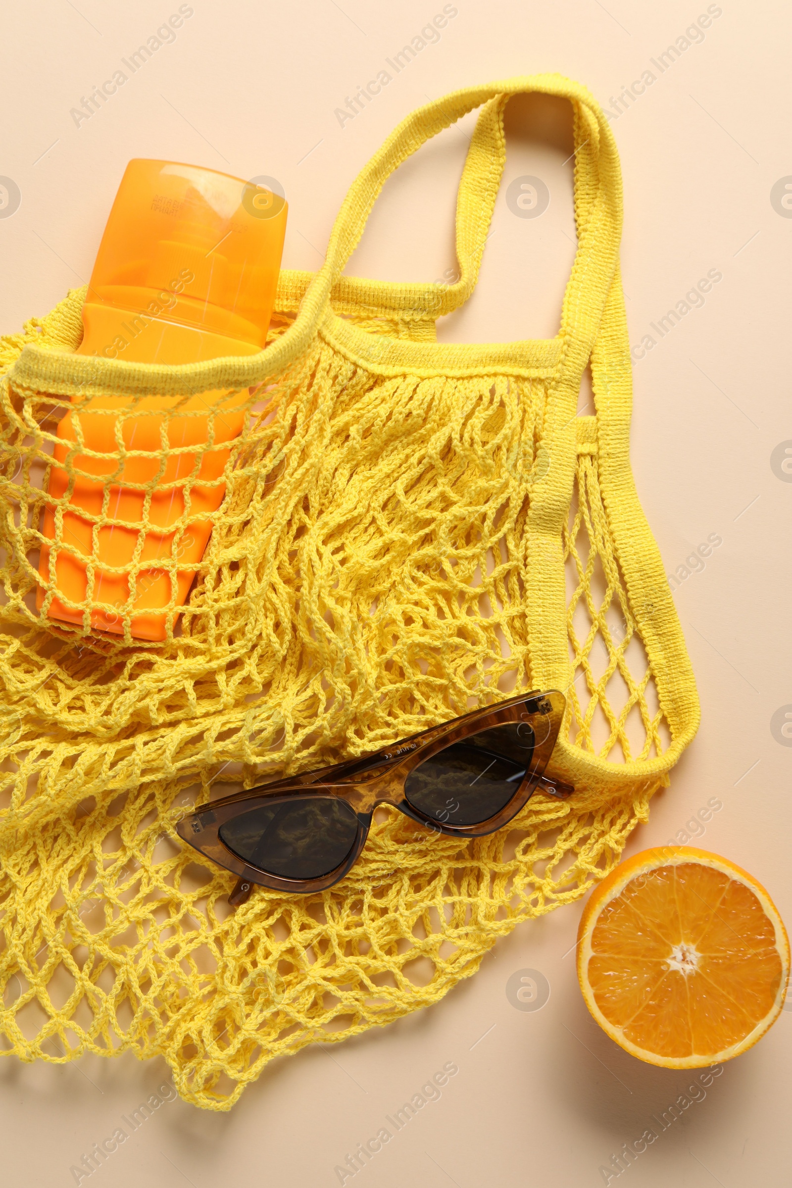 Photo of String bag, sunglasses, orange and sunscreen on beige background, top view