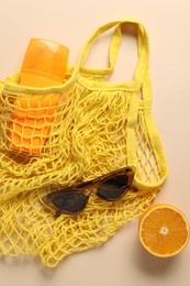 String bag, sunglasses, orange and sunscreen on beige background, top view