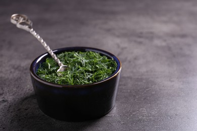 Fresh cut dill and spoon in bowl on grey textured table, closeup. Space for text