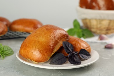 Photo of Delicious baked pirozhki and basil on light grey marble table, closeup