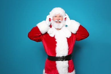 Santa Claus listening to Christmas music on color background