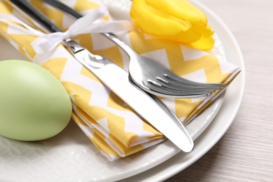 Photo of Festive Easter table setting with painted egg and floral decor on light wooden background, closeup