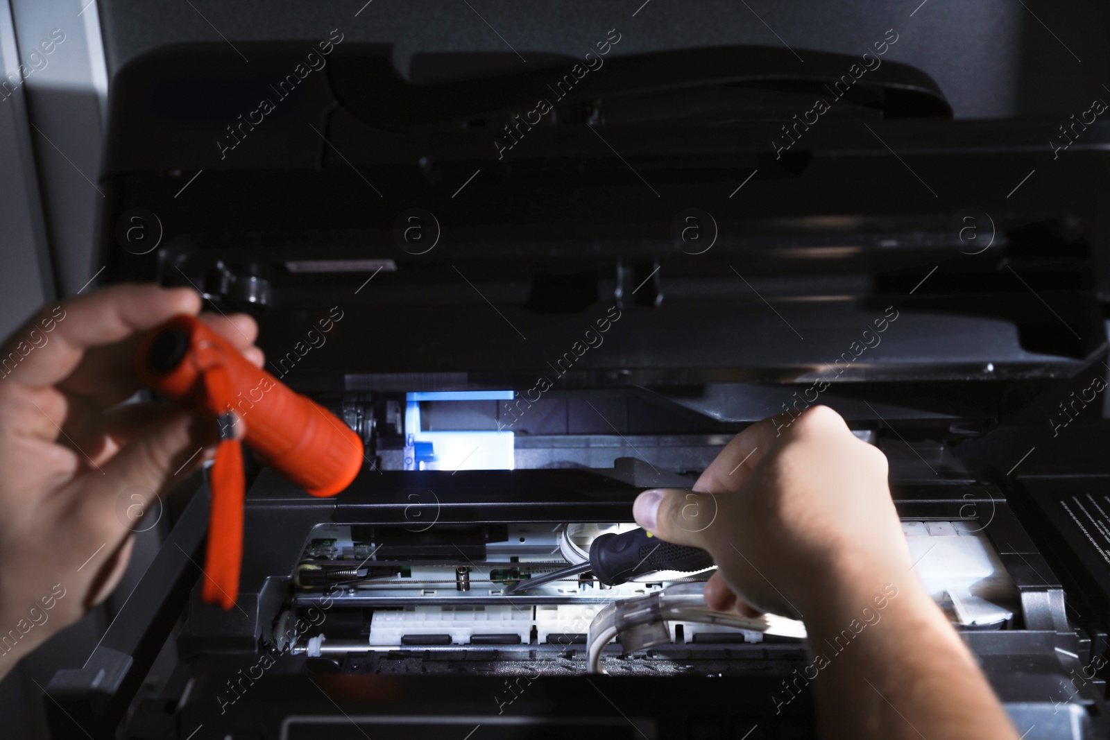 Photo of Repairman with flashlight fixing modern printer indoors, closeup