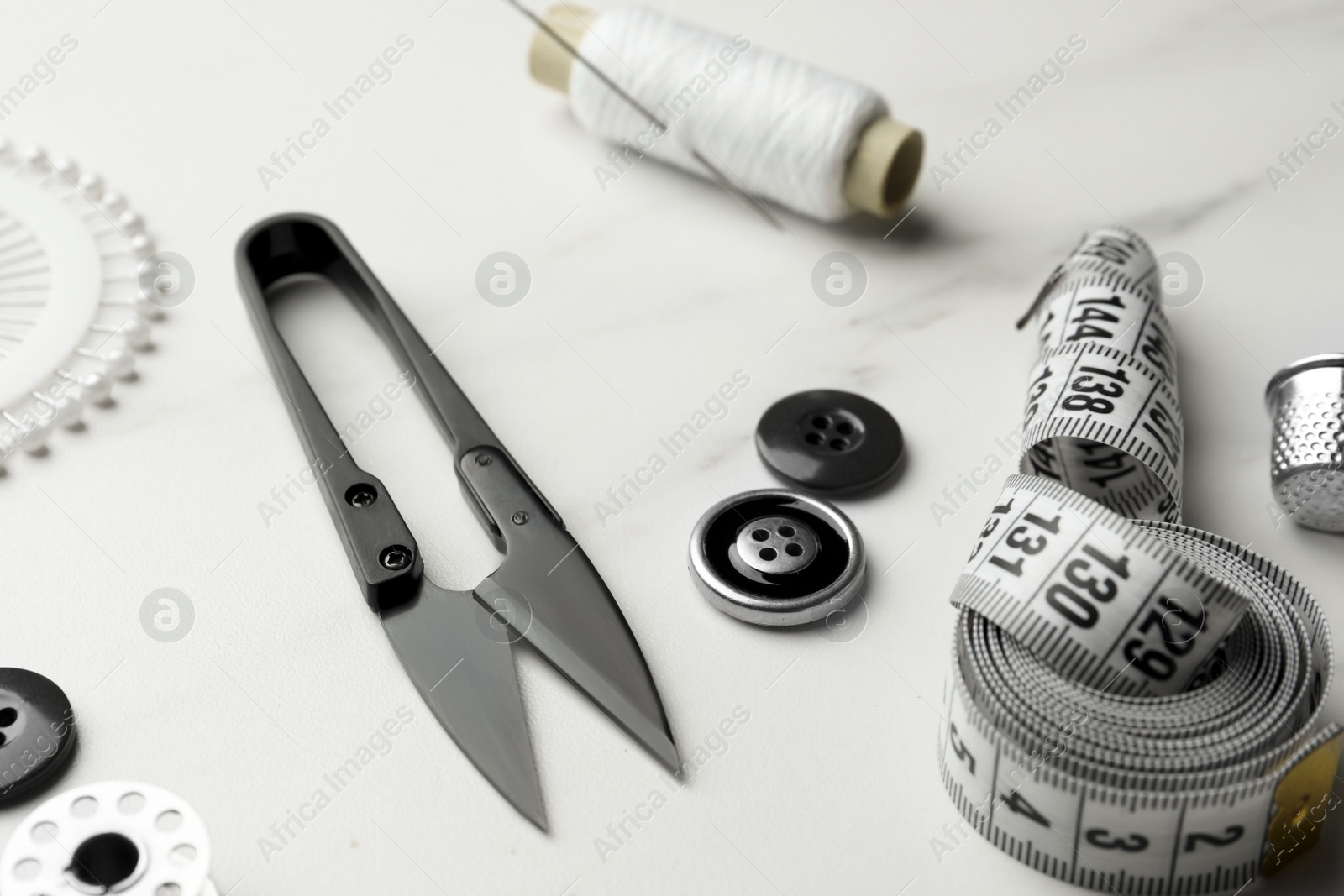 Photo of Thread and other sewing supplies on white marble table, closeup