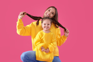 Young mother and little daughter on pink background