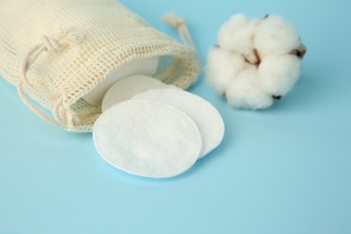 Photo of Bag with cotton pads and flower on light blue background, closeup