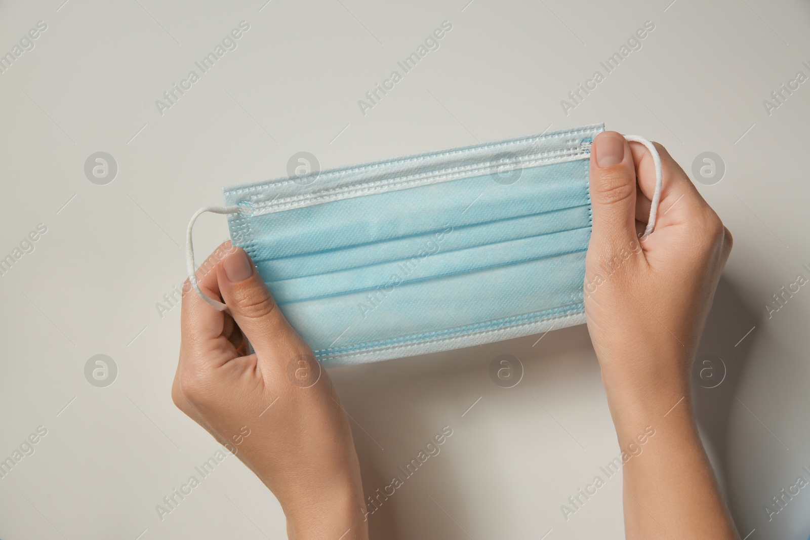 Photo of Woman holding disposable face mask on light background, closeup. Protective measures during coronavirus quarantine