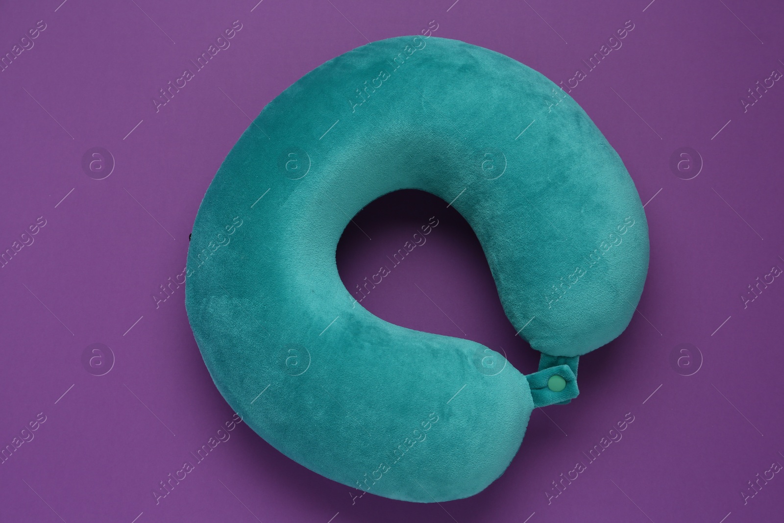 Photo of Turquoise travel pillow on purple background, top view