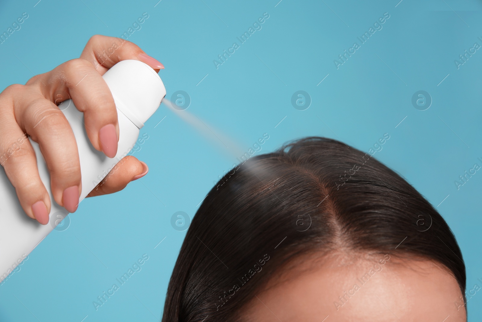 Photo of Young woman applying dry shampoo against light blue background, closeup
