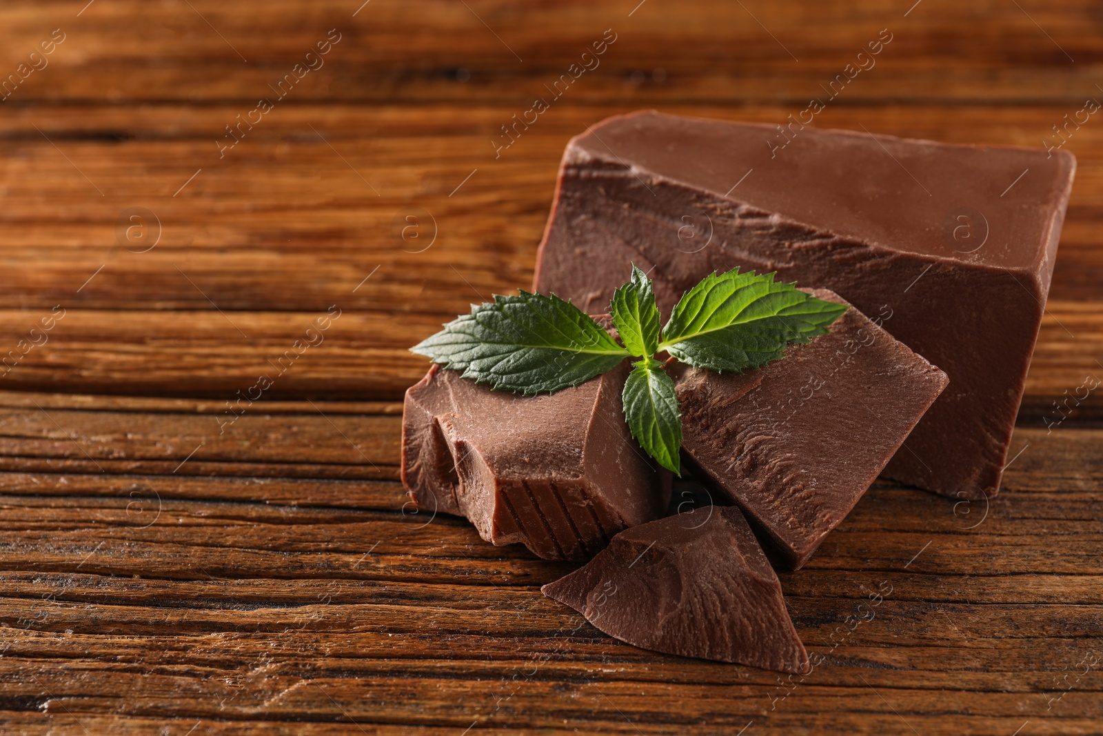 Photo of Pieces of tasty milk chocolate and mint on wooden table, closeup. Space for text