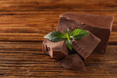 Pieces of tasty milk chocolate and mint on wooden table, closeup. Space for text