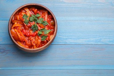 Bowl of delicious lecho with parsley on light blue wooden table, top view. Space for text