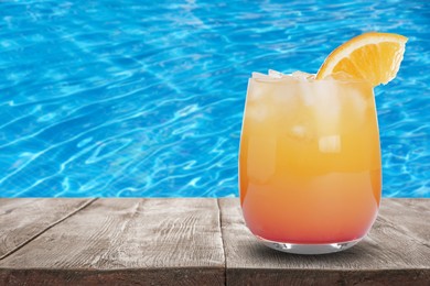 Image of Tasty refreshing cocktail on wooden table near outdoor swimming pool, space for text