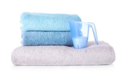 Laundry detergent in plastic measuring cup and towels on white background