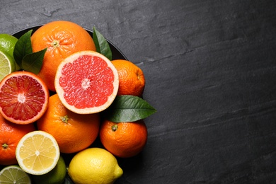 Different citrus fruits on black table, top view. Space for text