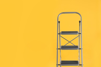 Modern metal stepladder on yellow background. Space for text