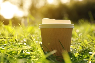 Photo of Paper cup on green grass outdoors, closeup. Coffee to go