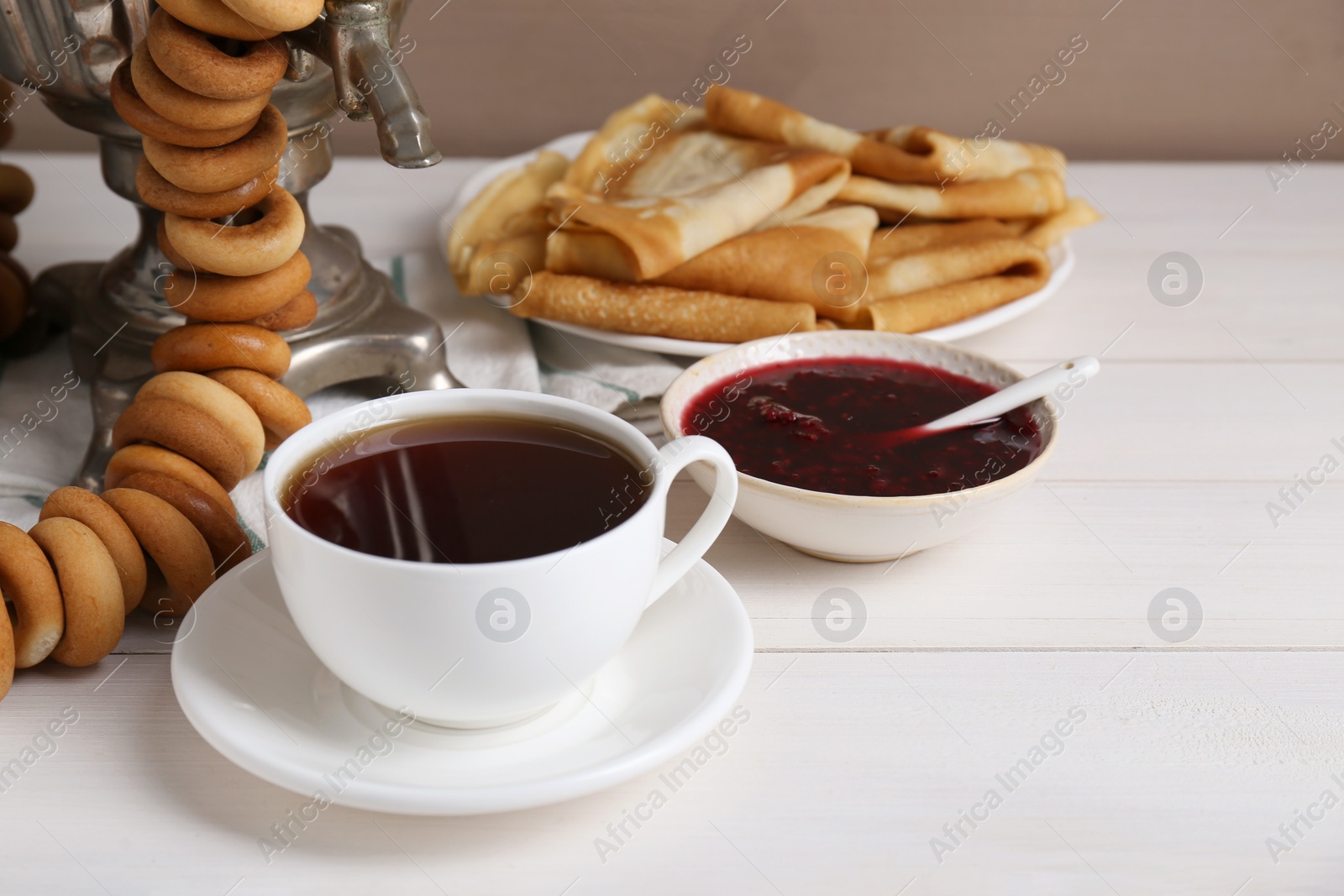 Photo of Metal samovar with cup of tea and treats on white wooden table, space for text