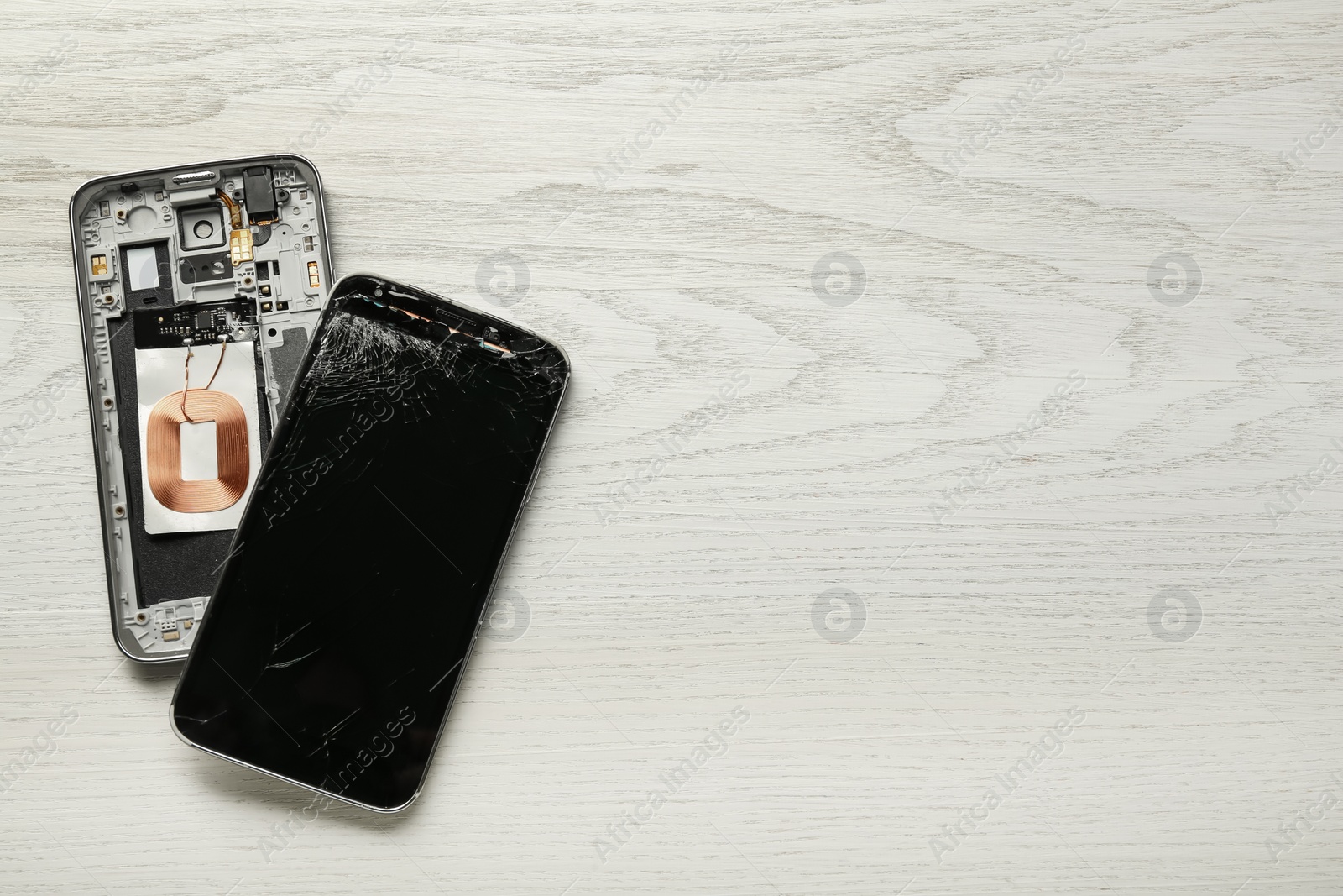 Photo of Damaged smartphone on wooden background, flat lay with space for text. Device repairing