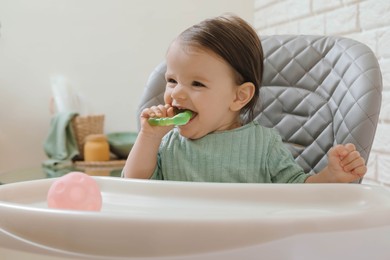 Photo of Cute little baby nibbling teether in high chair indoors. Space for text