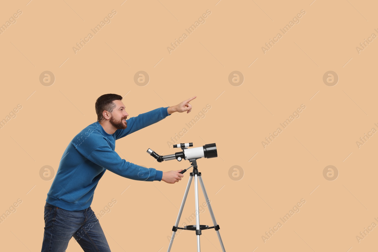 Photo of Happy astronomer with telescope pointing at something on beige background. Space for text