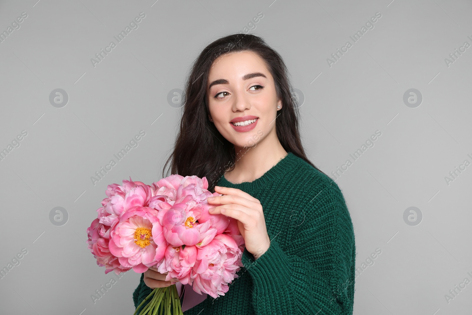 Photo of Beautiful young woman with bouquet of peonies on light grey background