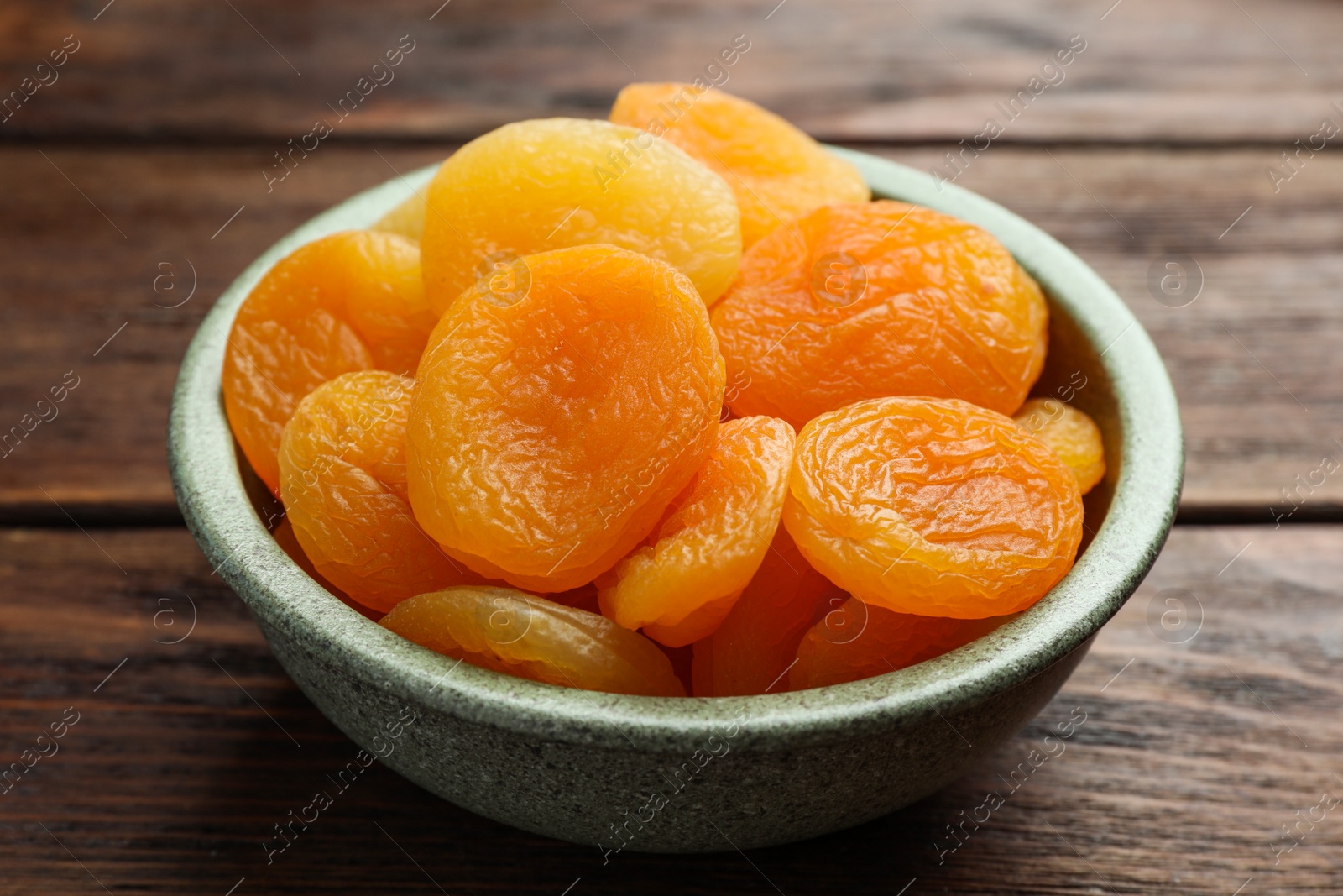 Photo of Bowl of tasty apricots on wooden table, closeup. Dried fruits