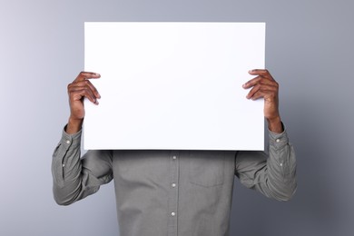 Photo of African American man holding sheet of paper on grey background, closeup. Mockup for design