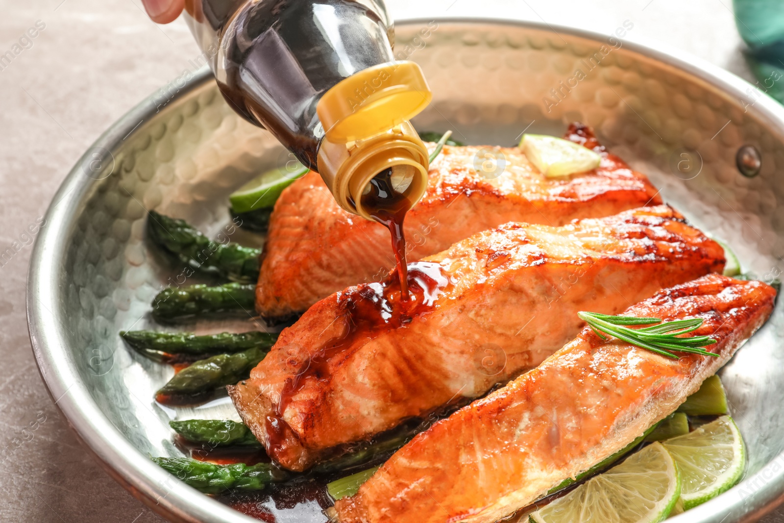 Photo of Pouring sauce onto tasty cooked salmon in frying pan, closeup